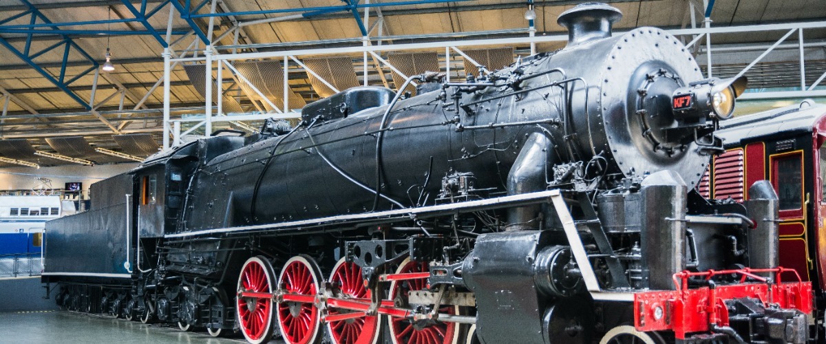Black steam train with red wheels set up in a museum showroom setting